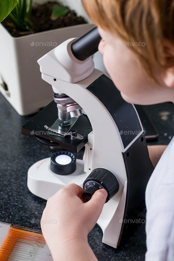 a teenager studying carefully glasses with laboratory materials under a microscope