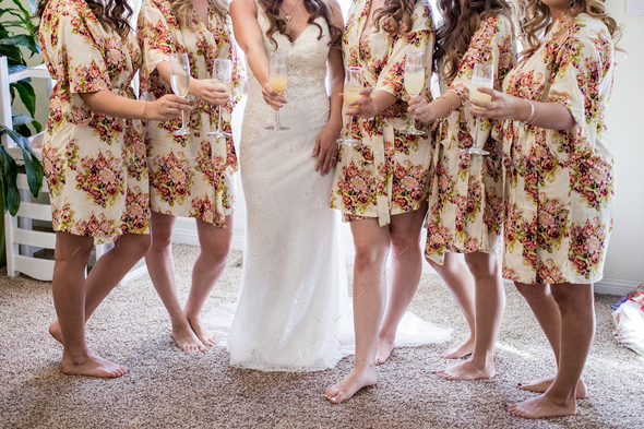 Bridesmaids dresses in flowered robes and bride dressed in her long gown make a toast to celebrate