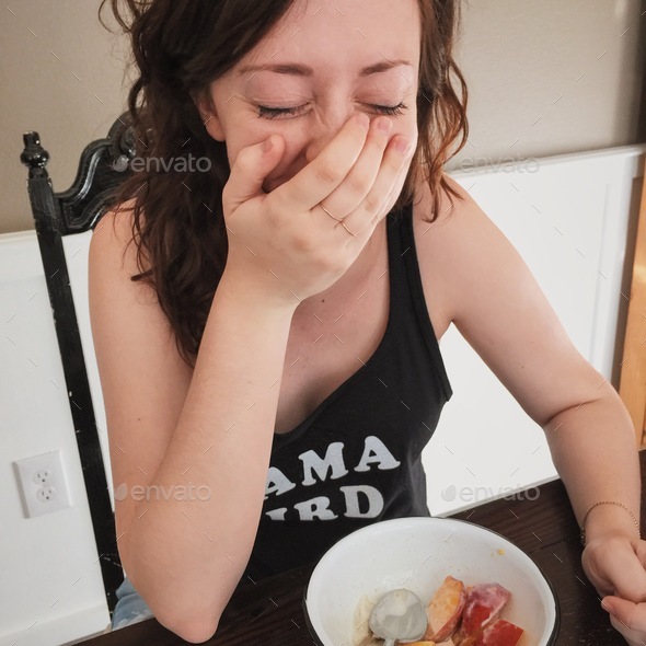 A young pregnant mom laughs and covers her mouth while eating ice cream and fresh peaches