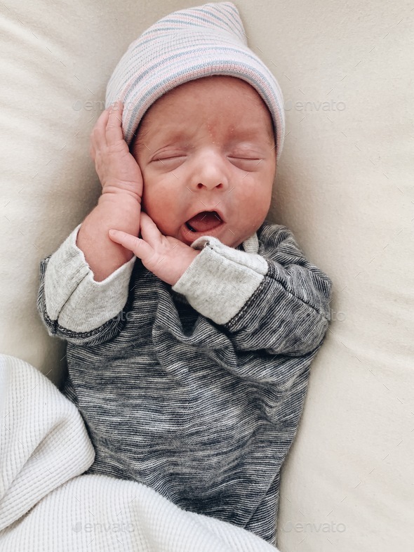 Newborn with a little hat sleeping with his hands up to his face Stock