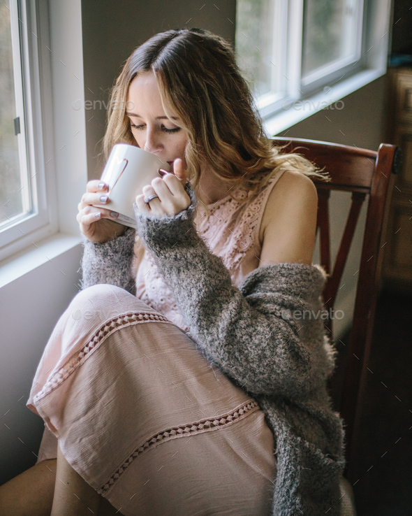 Young woman taking some time to relax with a cup of tea by a window  - Stock Photo - Images