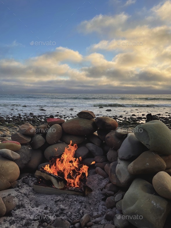 Wood burning fire pit on a rocky beach at golden hour - Stock Photo - Images