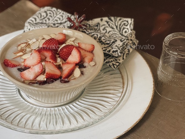 Hot oatmeal cereal with strawberries, almonds, cranberries and almond milk in a stoneware bowl - Stock Photo - Images