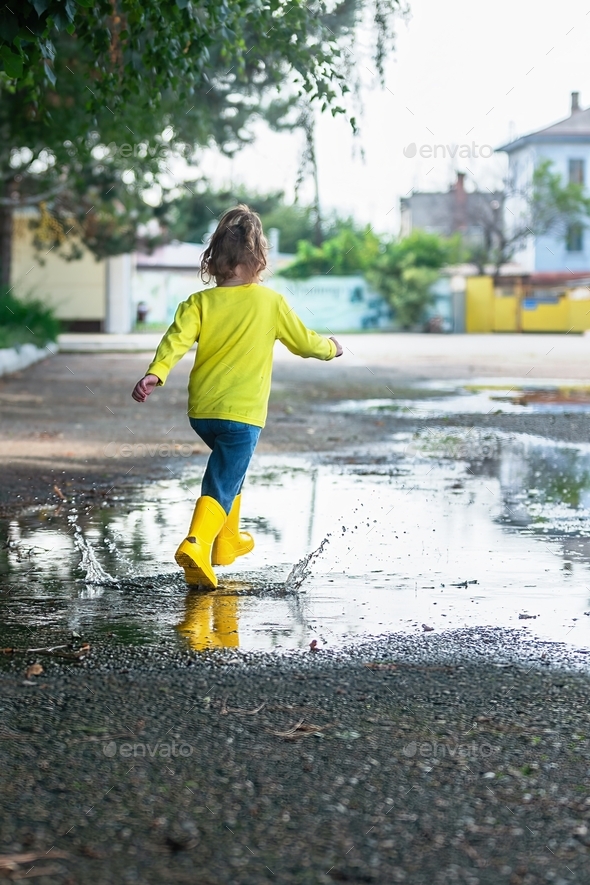 a little active girl on a walk after the rain runs through the puddles