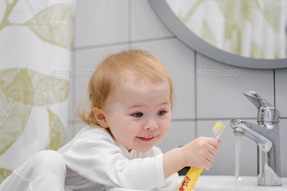 A funny cute toddler making face brushing teeth in bathroom. Learning ...