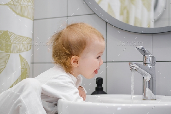 A kid learning morning hygiene routine. A toddler washing hands in sink ...