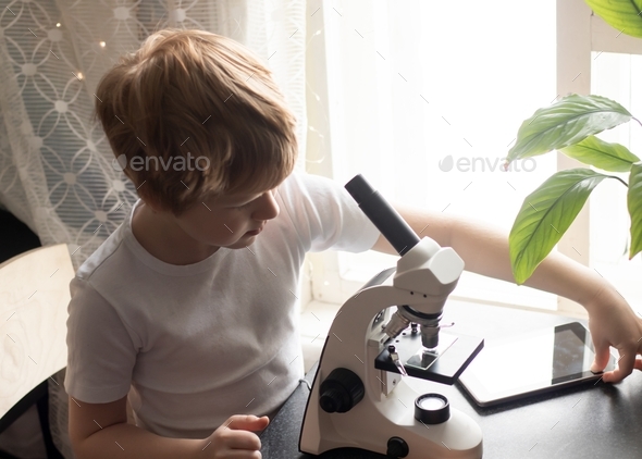 a child studying glasses with laboratory materials under a microscope and using mobile device