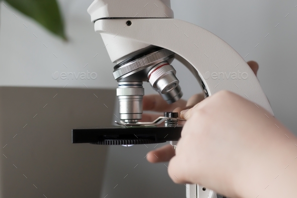 Close-up of a child's hands studying glasses with laboratory materials under a microscope