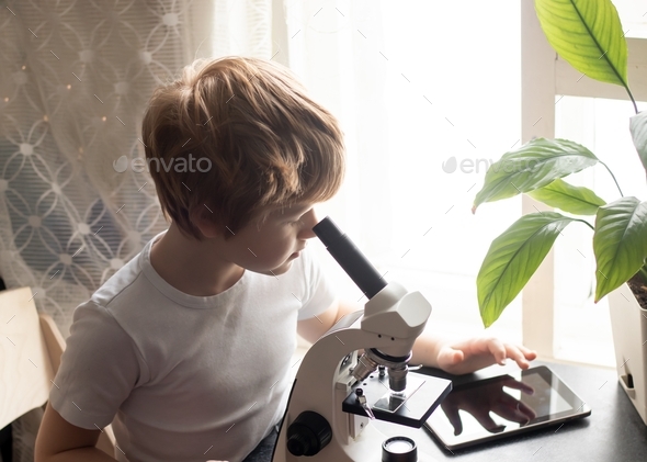 a child studying glasses with laboratory materials under a microscope and using mobile device