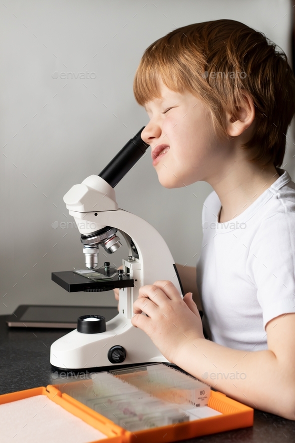 Close-up of a boy child studying glasses with laboratory materials under a microscope