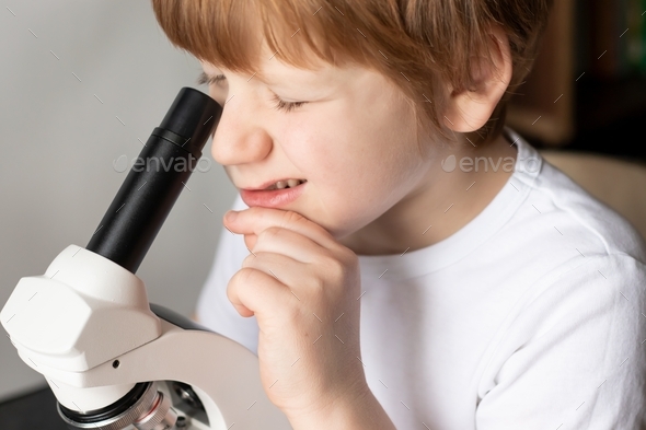 Close-up of a boy\'s face studying glasses with laboratory materials under a microscope