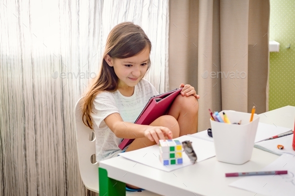 School age girl sitting at the messed desk and looking at hamster. Gen Z girl using a tablet.