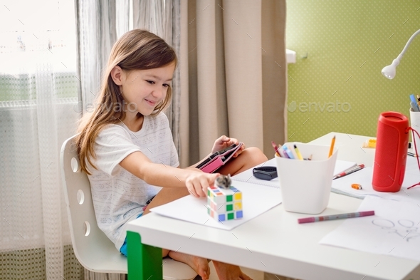 School age girl sitting at the messed desk and caressing hamster. Gen Z girl using a tablet.