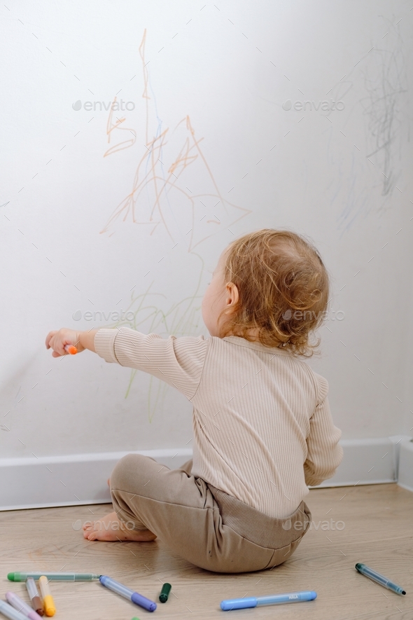 A toddler drawing on the white wall using colored marker. Child development of imagination.