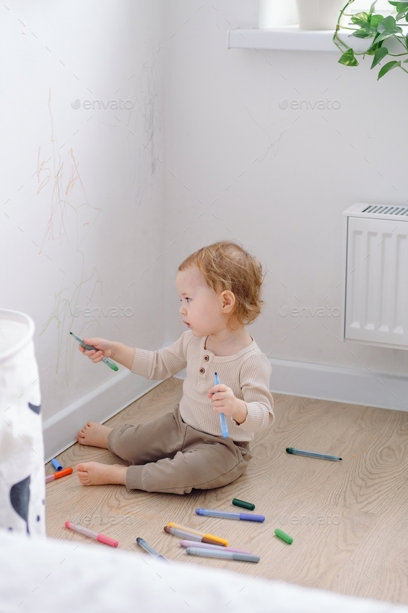 A toddler painting on the white wall using colored marker. Child development of imagination.