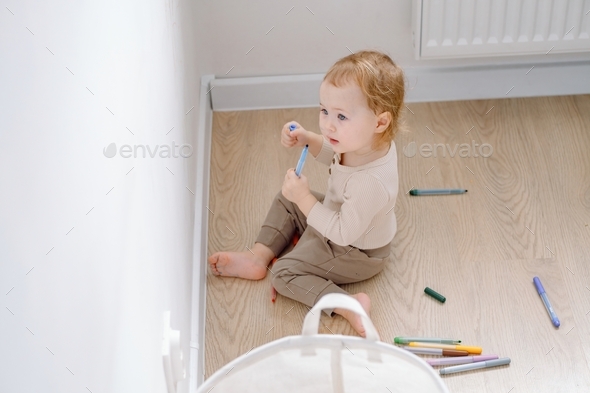 A toddler holding colored marker ready to draw on the white wall. Developing imagination and art.