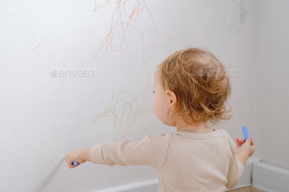 A toddler drawing on the white wall using colored marker. Child development of imagination.
