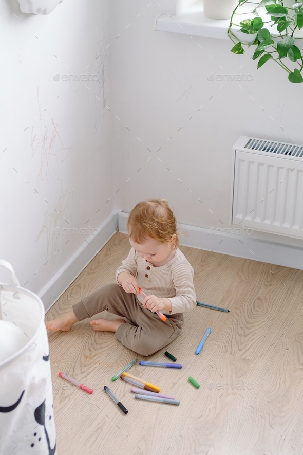A toddler holding colored marker ready to draw on the white wall. Developing imagination and art.