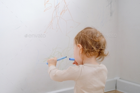 Close up of a toddler drawing on white wall using colored marker. Child development of imagination.