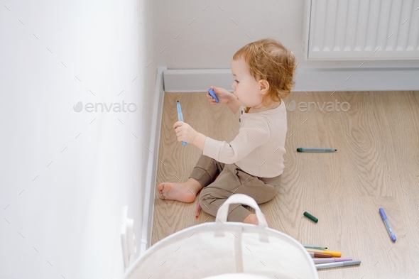 Child development of imagination. A toddler drawing on the white wall using colored marker.
