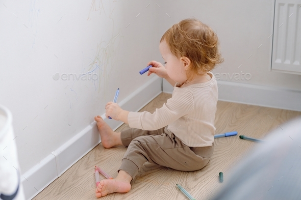 Developing kid’s imagination. A toddler drawing on the white wall using colored marker.