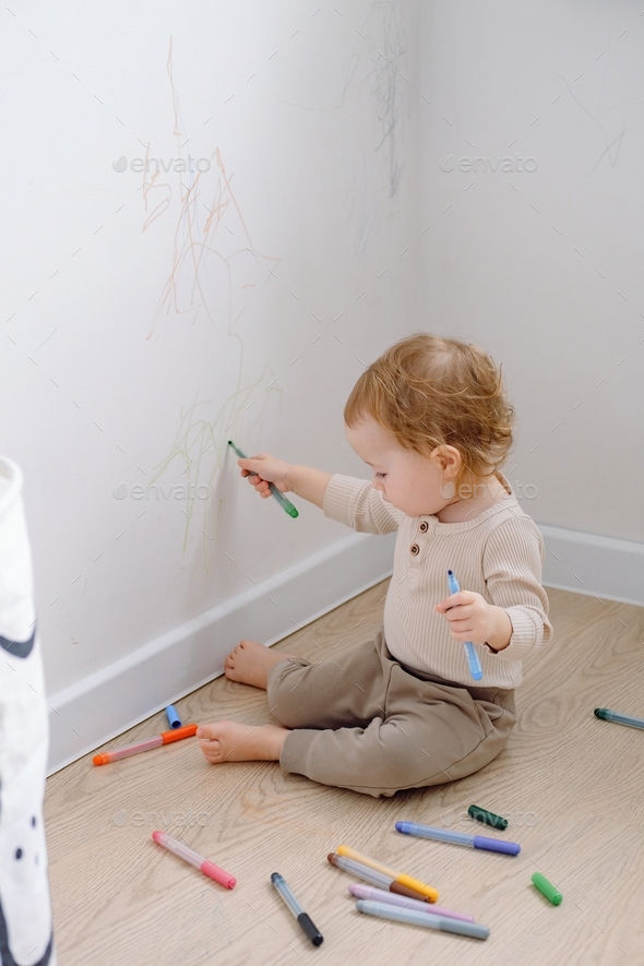 Developing imagination. A toddler drawing on the white wall using colored marker. Allowing children.