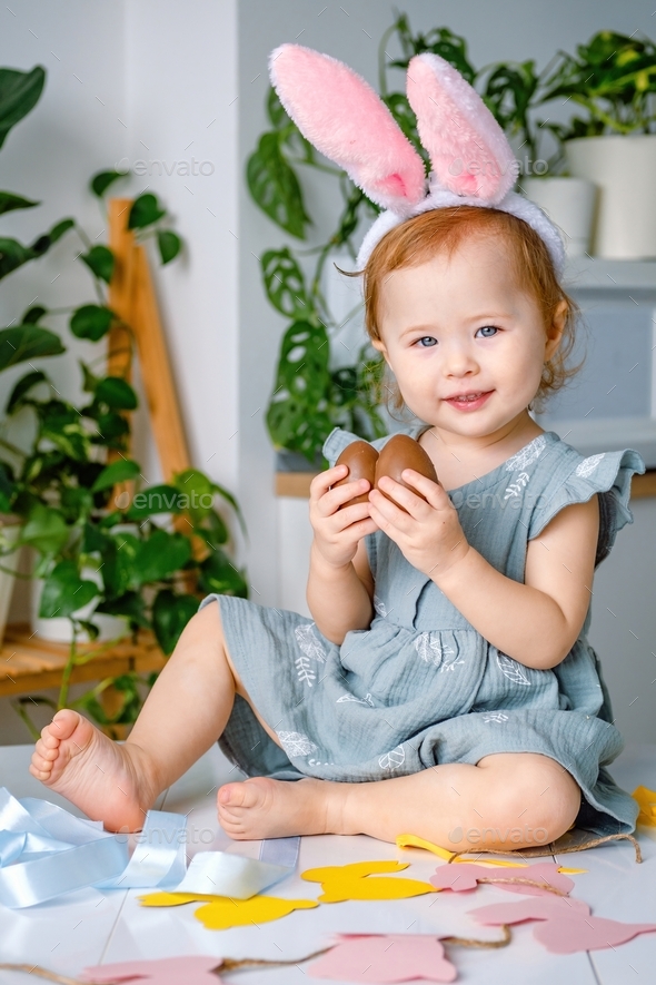 A cute smiling cheerful toddler girl dressed up bunny ears holding easter gift chocolate eggs. - Stock Photo - Images