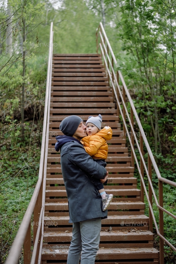 Happy father holds his child and kisses. A dad and toddler on walk in the park forest on cold day. - Stock Photo - Images