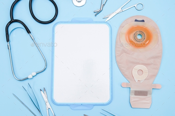 Colostomy bag, surgical instruments, stethoscope and bandages lie around an marker board on a blue .