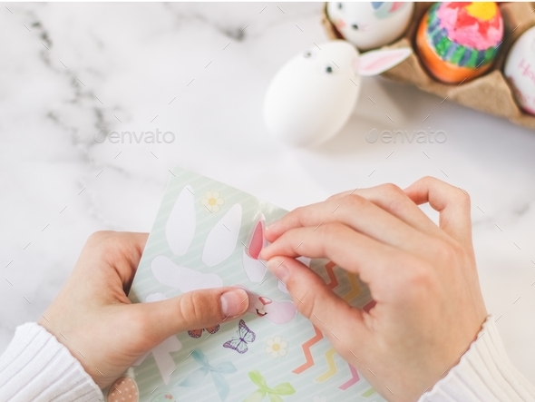 Children's hands hold stickers and peel off easter egg bunny ears with fingers, sit at marble table