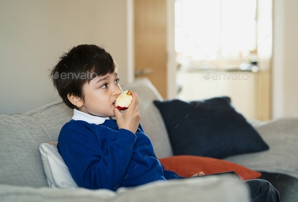 Healthy child eating red apple,School boy eating fresh fruit for his snack while watching TV  - Stock Photo - Images