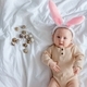 Cute funny baby with bunny ears dressed up for Easter laying on white bed sheet with quail eggs.  - PhotoDune Item for Sale