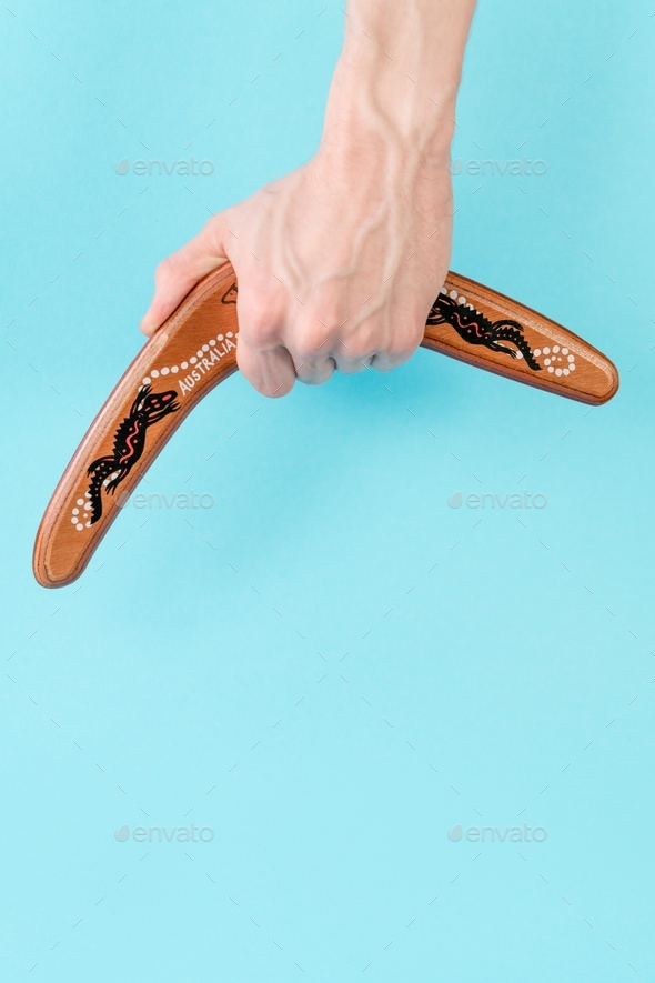 wooden boomerang in a man\'s hand closeup on a blue background with free space for text