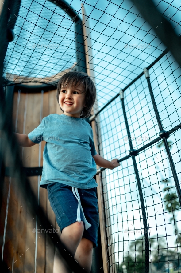 a child walks on an alpine grid on a children's playground, a boy walks in the park in summer - Stock Photo - Images