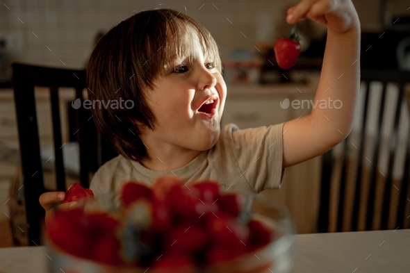 the boy happily looks at the strawberries. A child eats a berry - Stock Photo - Images