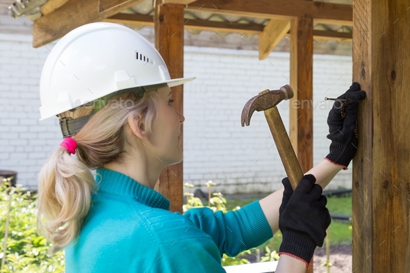 Woman hammering a nail into a wooden post