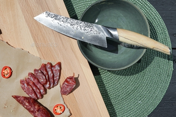 Sharp chef's knife close up on the cutting board and sliced smoked sausage. - Stock Photo - Images