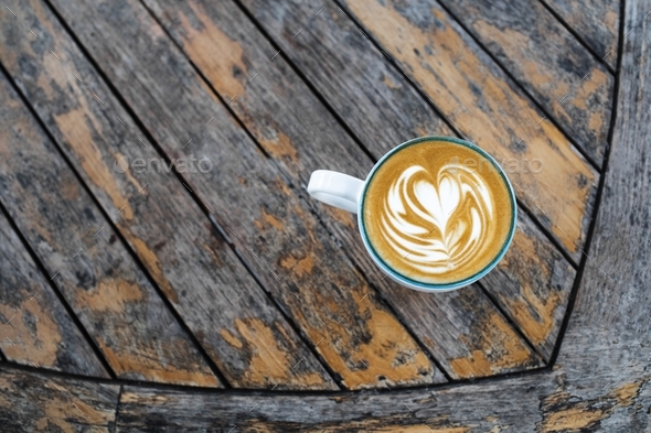 Cup of fresh creamy cappuccino with latte art on foam. Background of wooden table with shabby aged - Stock Photo - Images