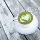Cup of fresh green matcha latte beverage with latte art on foam. Background of wooden table - PhotoDune Item for Sale