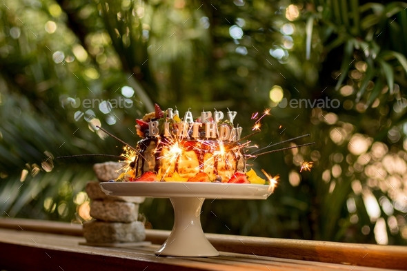 Delicious handmade layered cake decorated with sparkles, happy birthday candles and fruits