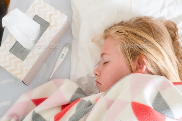 Sick teenage girl lying on the bed covered with blanket with thermometer