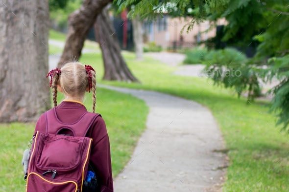 Back to school. Girl wearing maroon school uniform and hat walking to school alone