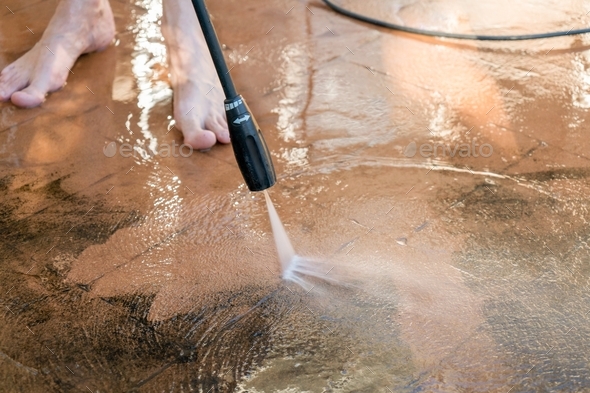 Man Washing dirty backyard tiles with high pressure cleaner. Spring clean up