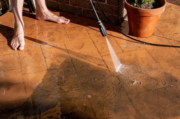 Man Washing dirty backyard tiles with high pressure cleaner. Spring clean up