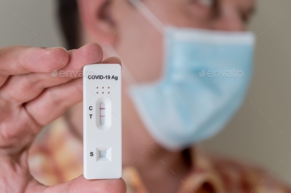 Man in face mask holding positive Covid-19 Antigen Rapid test result. rapid diagnostic test
