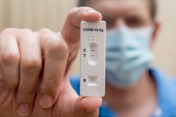 Man wearing face mask with positive Covid-19 Antigen Rapid test result. Rapid diagnostic test.
