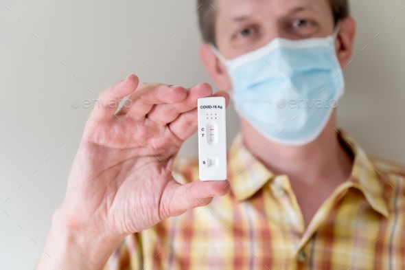 Man in face mask holding positive Covid-19 Antigen Rapid test result. rapid diagnostic test