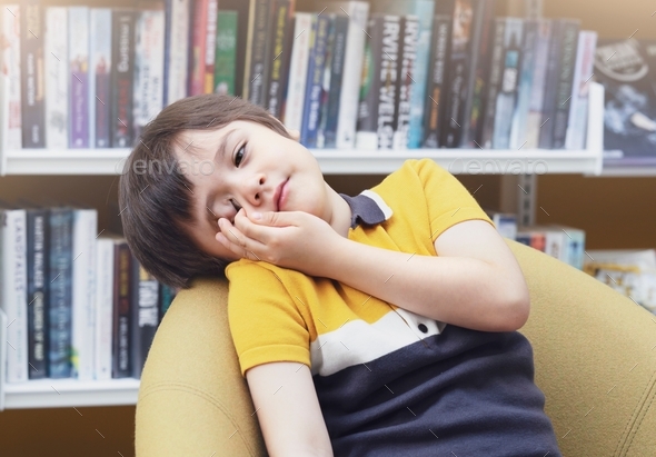 Tried boy rubbing his eyes while sitting in school library, bored kid fall asleep