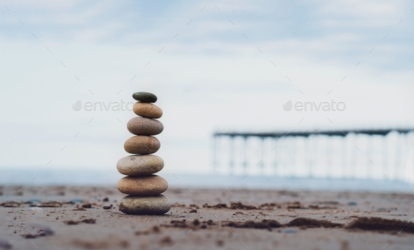Pebble tower by the seaside with blurry pier down to the sea, Stack of zen rock stones on the sand,