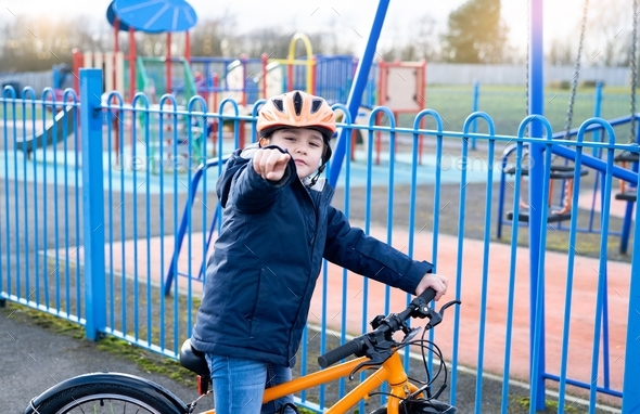 Kid pointing finger out, School kid learns to ride a bike in the Park, Portrait of boy on bicycle